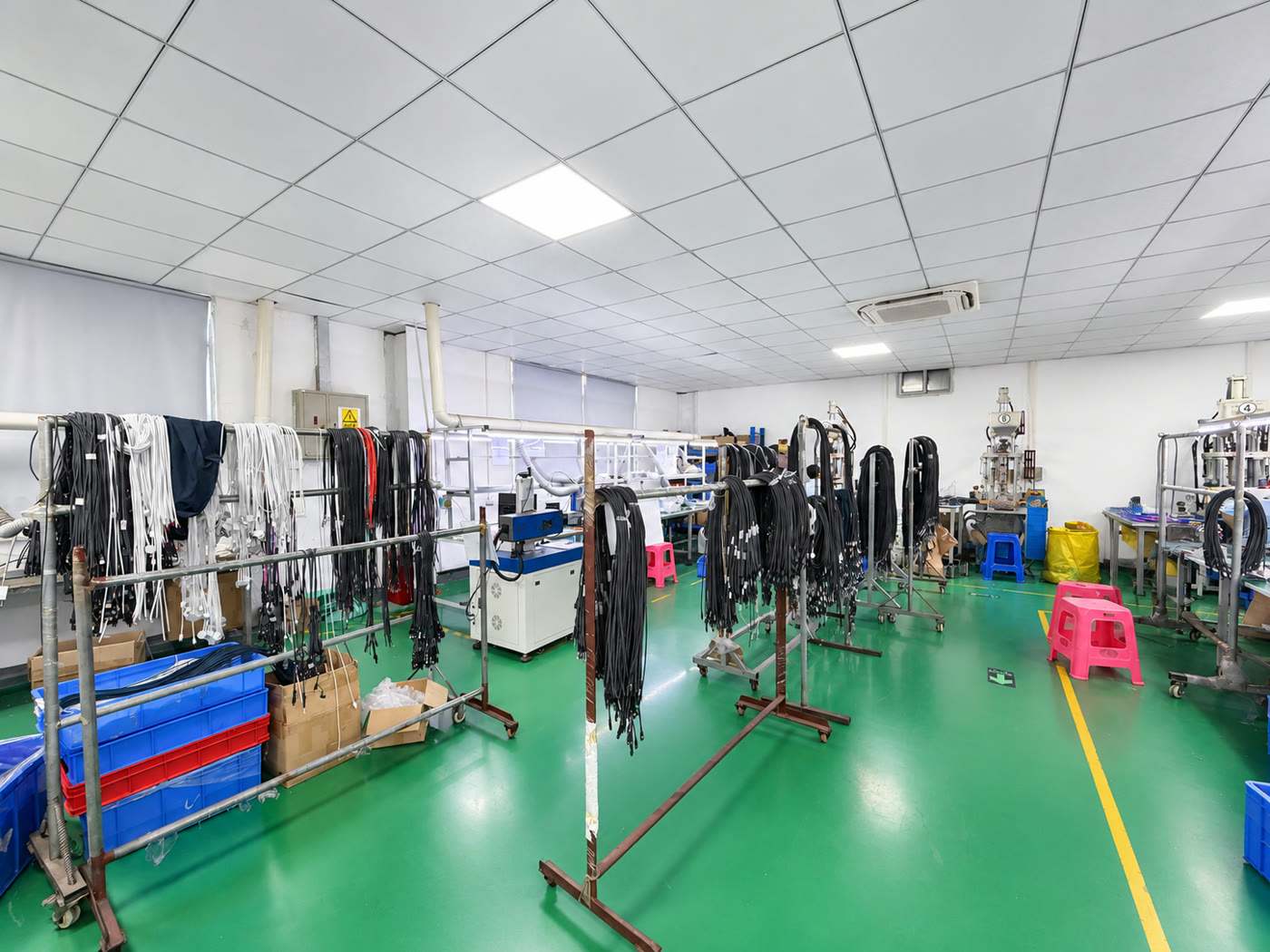 Cable workshop with black and white cable assemblies on movable racks, workbenches and production equipment