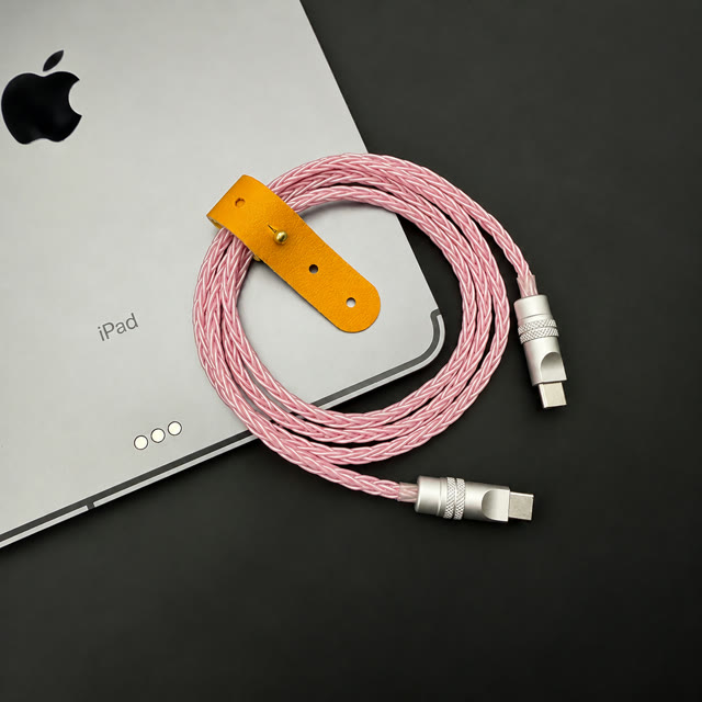 Pink twisted-wire USB-C cable with silver connector housings beside a tablet